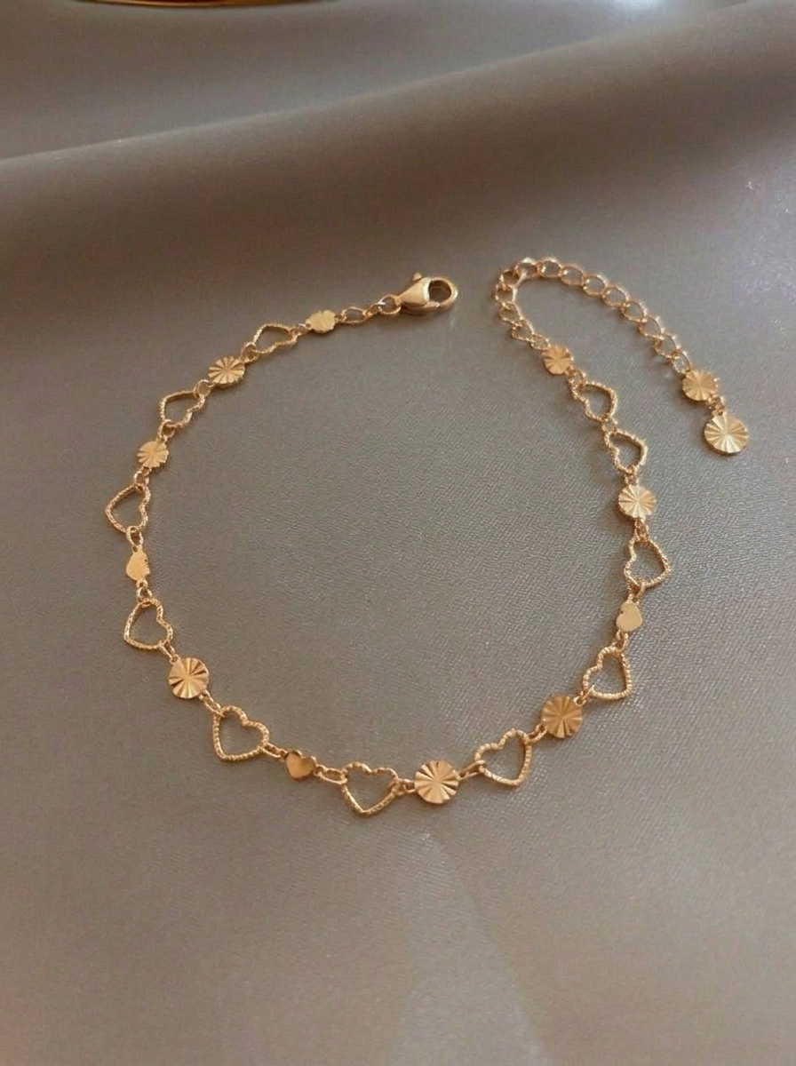 Cupid Heart Link Bracelet featuring open-heart gold links alternating with round textured sunburst discs on a smooth neutral surface