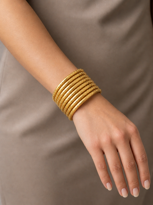 Close-up of a wrist wearing the Heera Stacked Sculptural Coil gold multi-layer wrap bracelet paired with a neutral beige dress