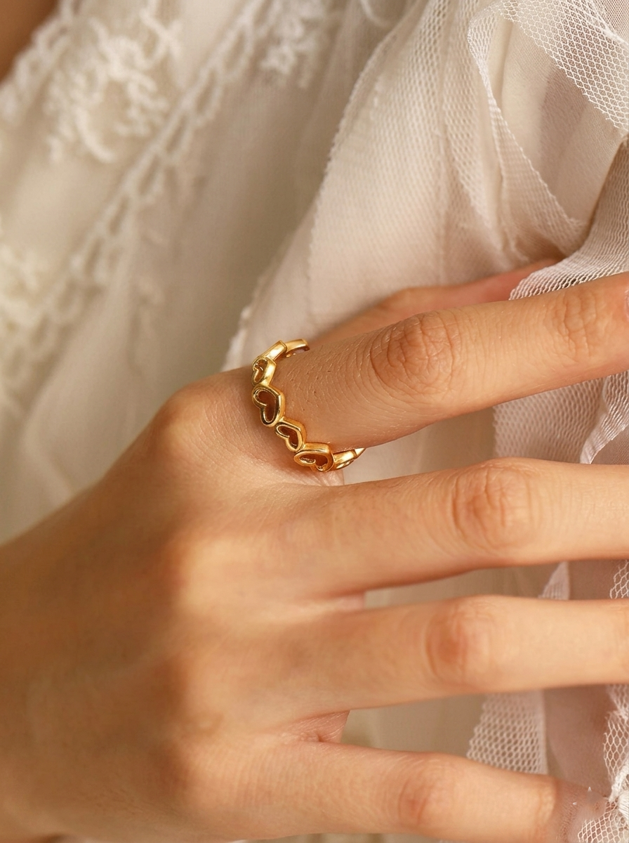 Close-up view of a hand wearing the Amora Heart Adjustable Ring gold heart band paired with delicate white lace fabric