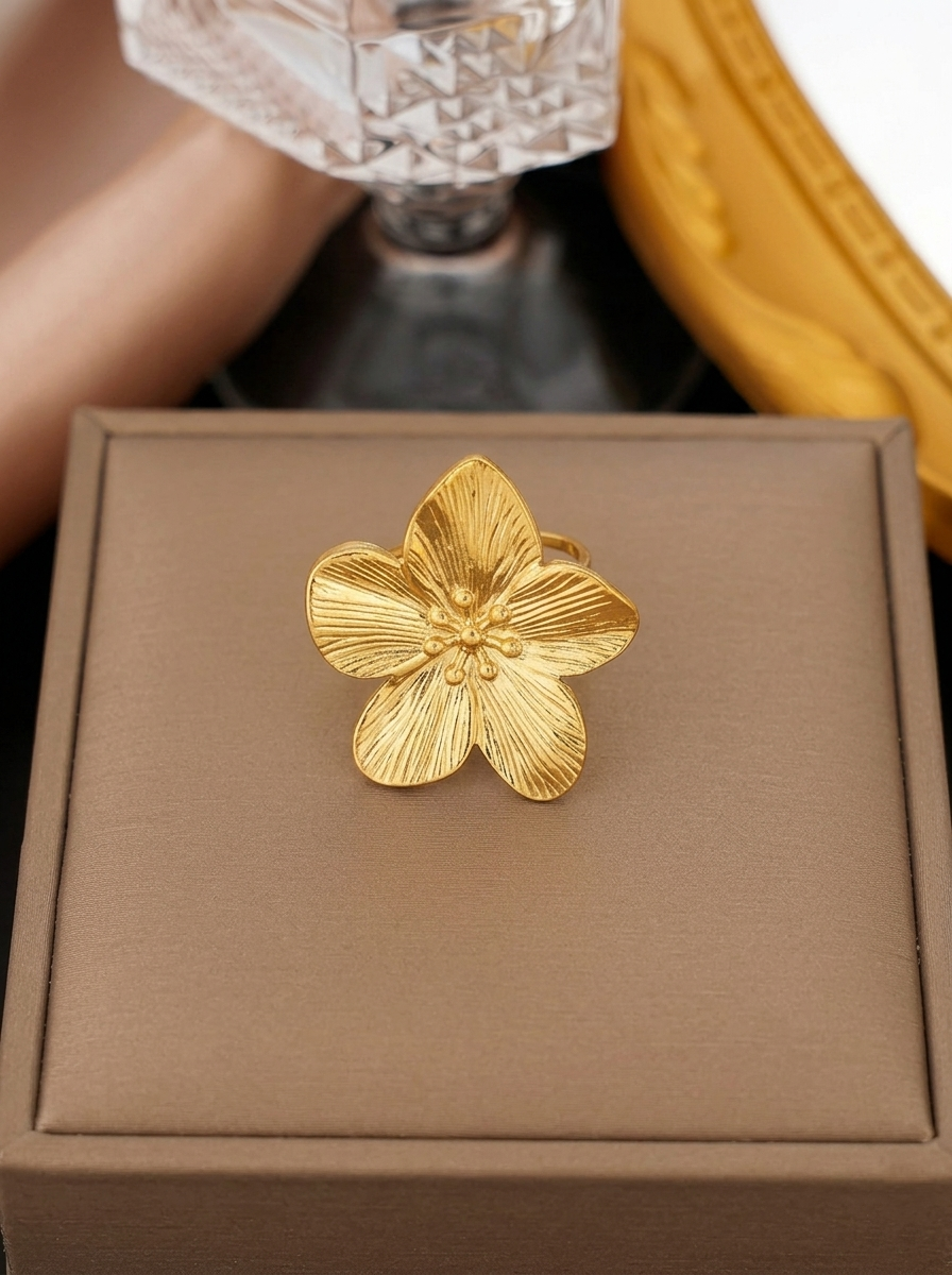 Hibiscus Molten Adjustable Ring featuring a large textured gold five-petal flower with detailed stamen accents resting on a beige jewelry display box