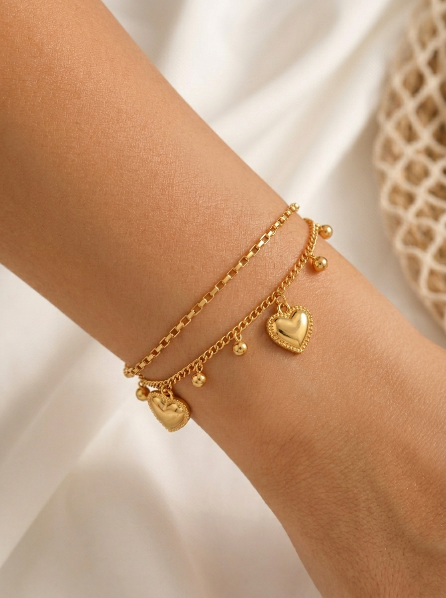 Close-up of a wrist wearing the Inaya Dual-Chain Heart Bracelet showcasing the layered gold chains with dangling heart and ball accents