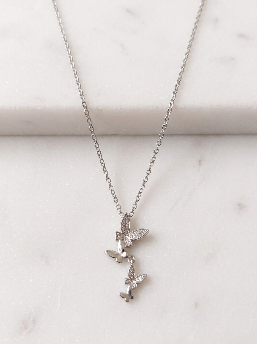 Mariposa Butterfly Pendant Necklace featuring a delicate silver chain and stacked cubic zirconia butterfly charms displayed on a clean white marble background