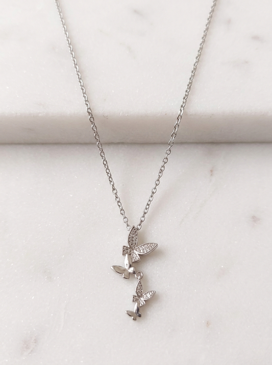 Mariposa Butterfly Pendant Necklace featuring a delicate silver chain and stacked cubic zirconia butterfly charms displayed on a clean white marble background