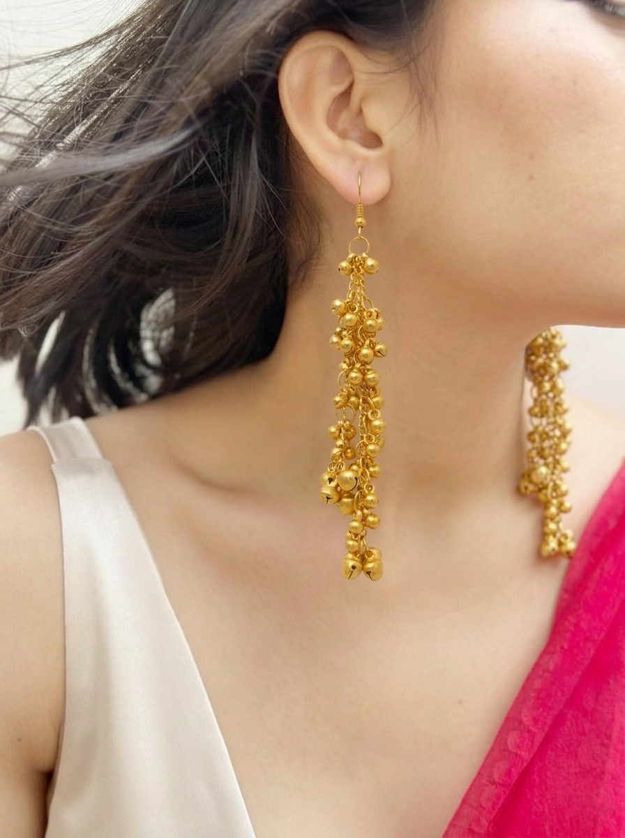 Side profile of a model wearing long Zaira Golden Ghungroo Drops dangling earrings paired with a white top and bright pink saree